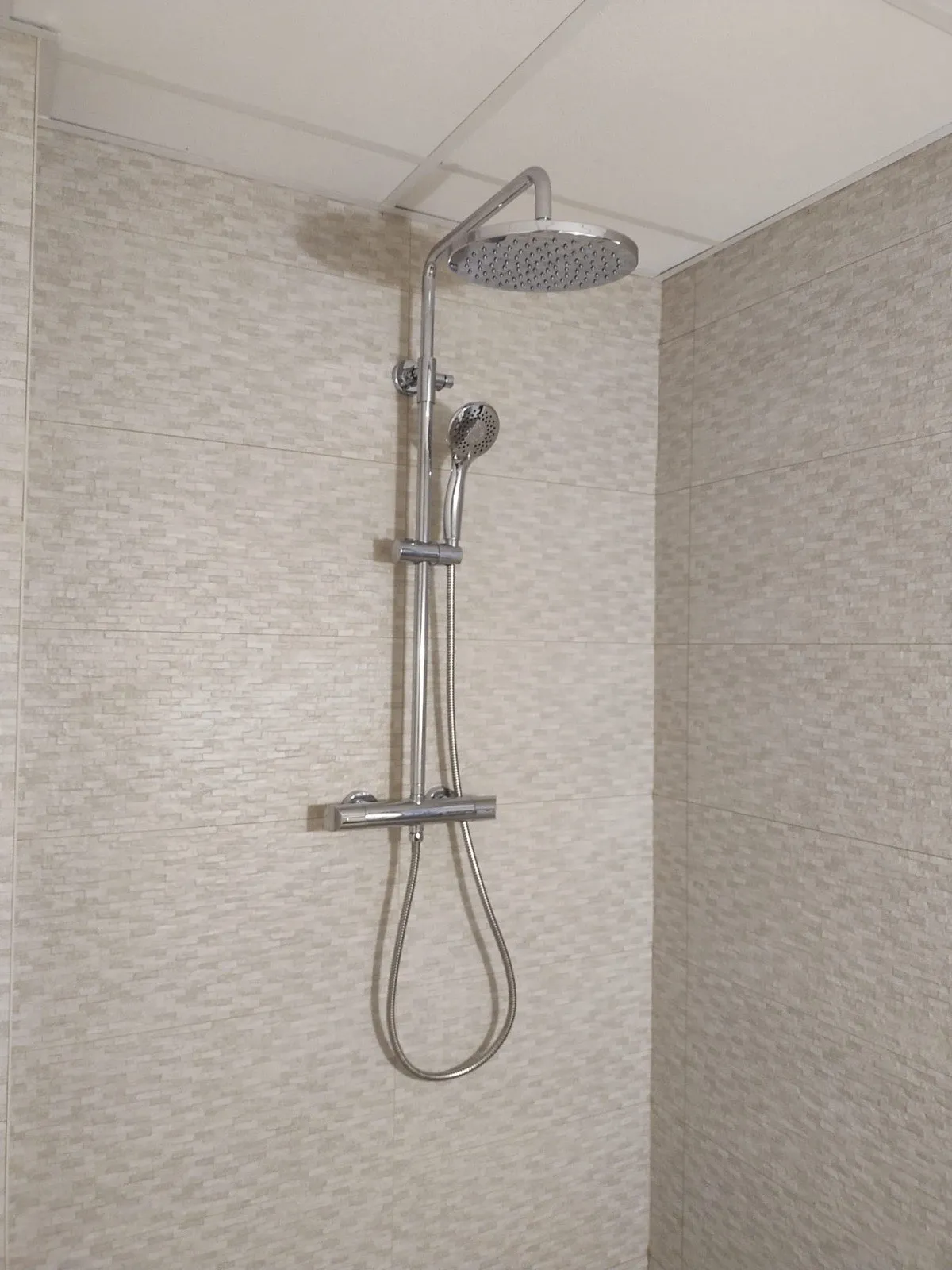 Columna de ducha con rociador cromado sobre alicatado beige texturizado en baño reformado