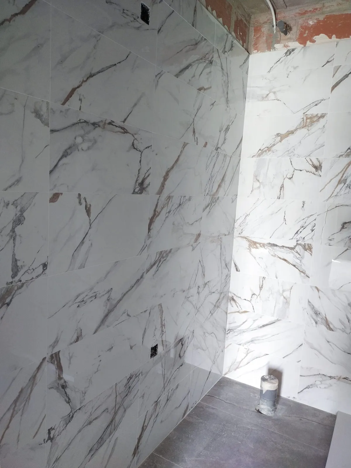 Baño en obra con paredes revestidas de porcelánico gran formato imitación mármol blanco con vetas doradas