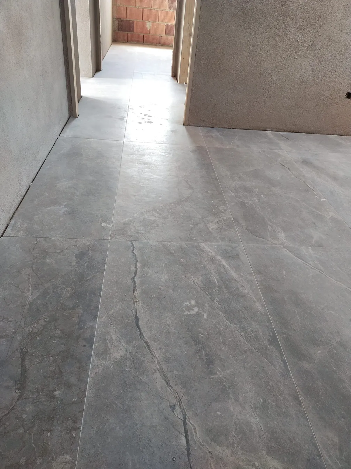 Pasillo con pavimento porcelánico gran formato efecto piedra gris recién colocado y paredes sin pintar