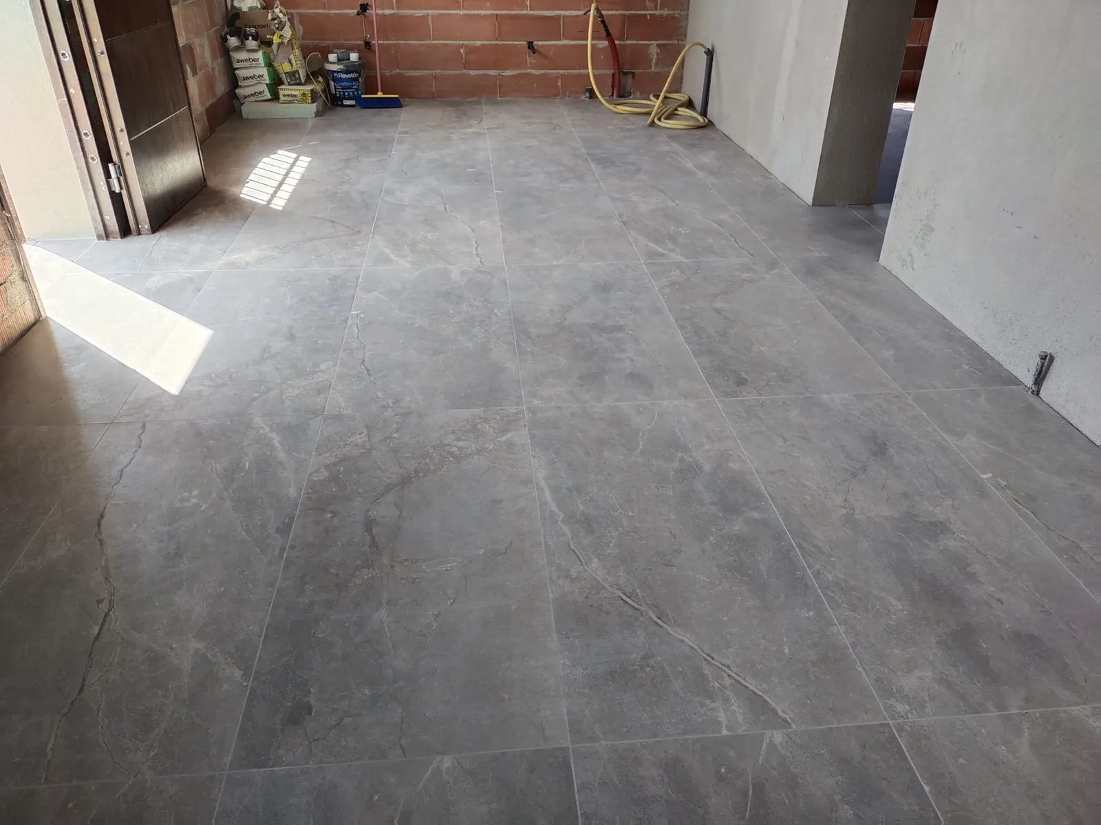 Estancia amplia en obra con suelo porcelánico efecto piedra gris y paredes de ladrillo vistas