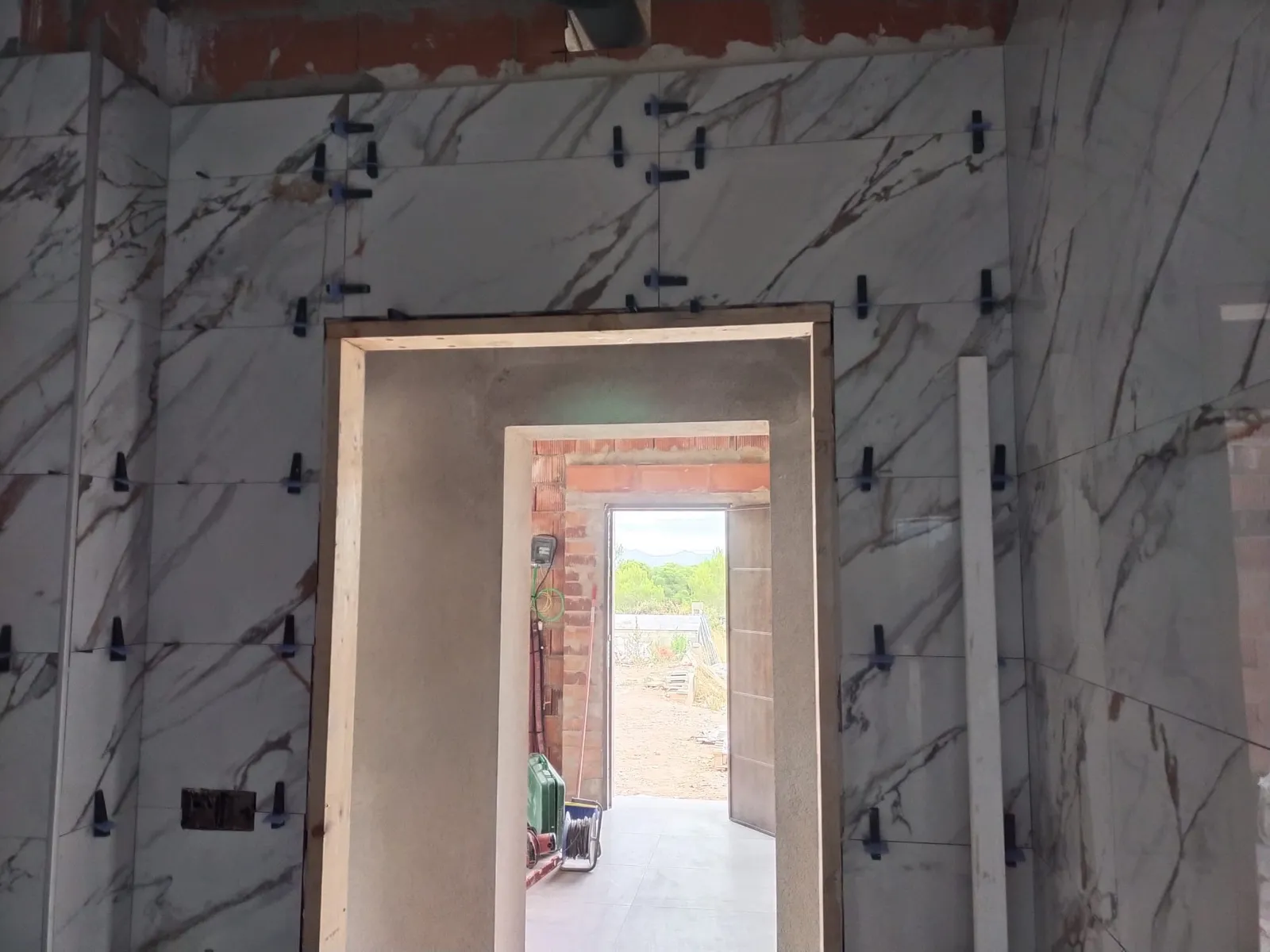 Baño en obra con alicatado imitación mármol y crucetas niveladoras junto a hueco de puerta