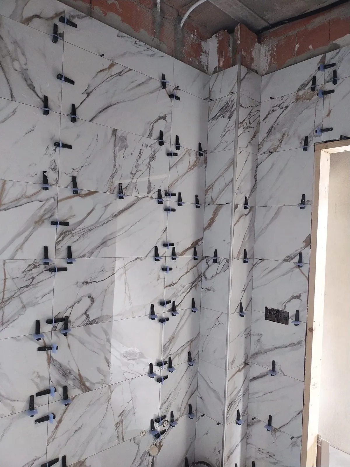 Detalle de alicatado porcelánico imitación mármol con crucetas niveladoras en baño en construcción