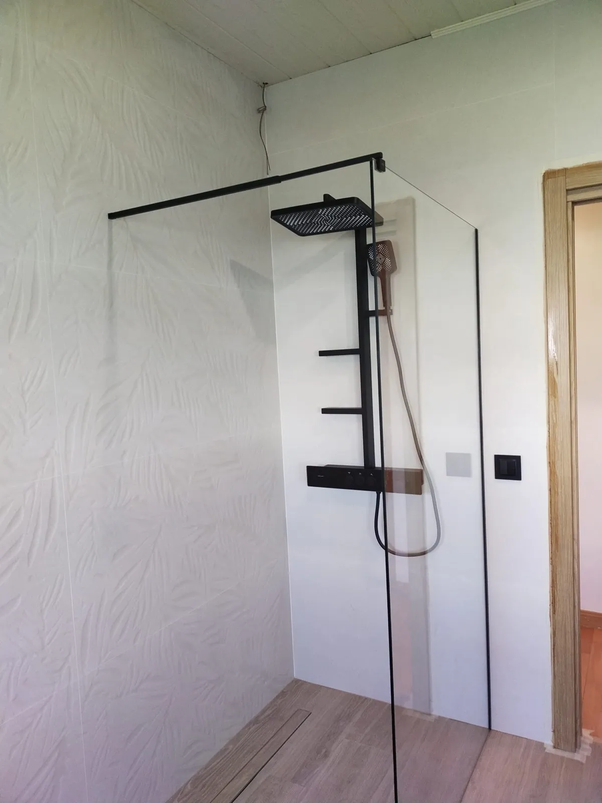 Ducha terminada en Tarragona con columna negra, azulejo blanco texturizado y suelo imitación madera