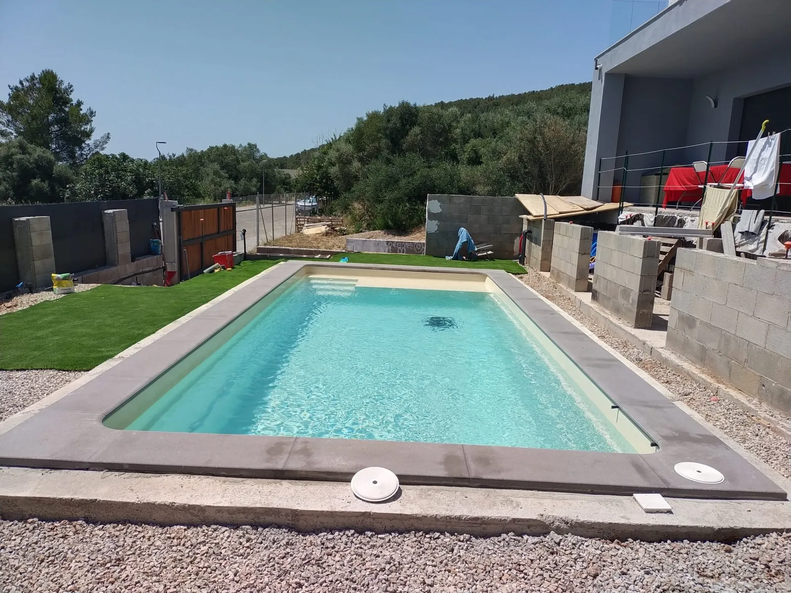 Piscina terminada con vaso en tono arena, corona de piedra gris oscuro y césped artificial
