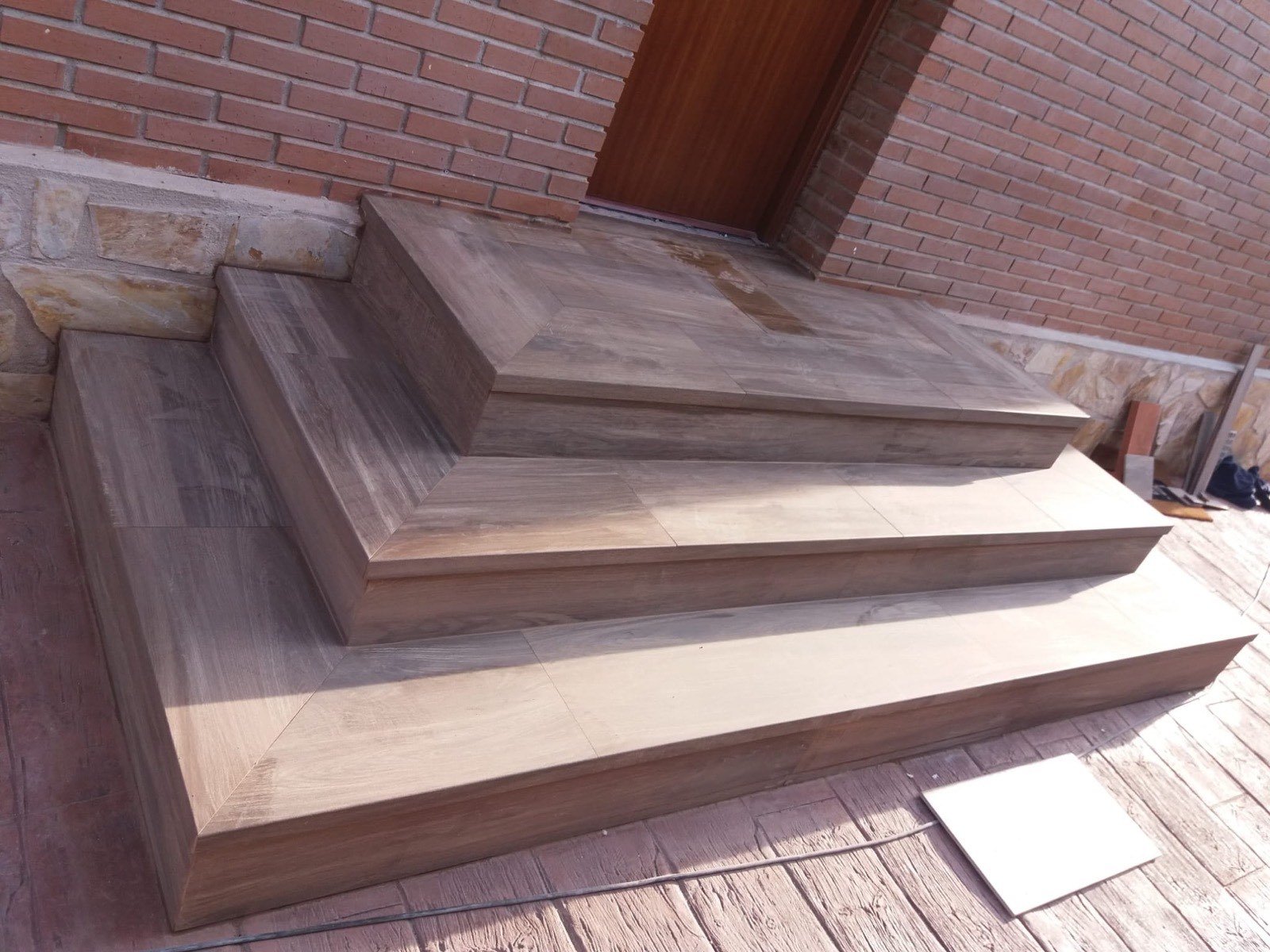 Esglaons exteriors revestits amb porcellànic imitació fusta al costat de façana de maó
